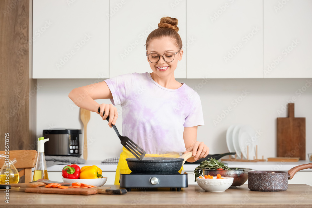 Wall mural Young woman frying vegetables in kitchen