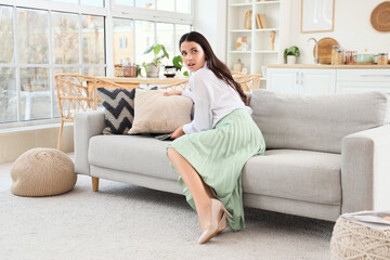 Beautiful woman hiding money under pillow on sofa at home