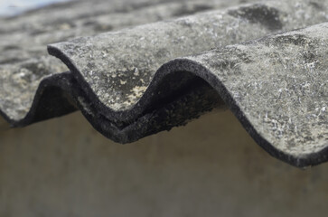 asbestos roof of building. extreme close up of wavy side edge of building roof. gray asbestos top cover texture, old and shabby