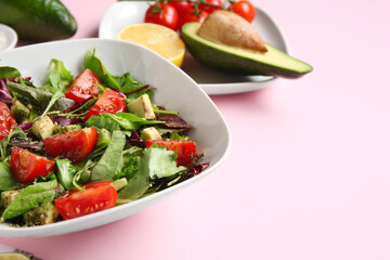 Bowl of tasty avocado salad with cherry tomatoes on pink background, closeup
