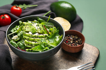 Bowl with tasty avocado salad with mozzarella cheese and ingredients on green background