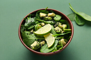 Bowl of tasty avocado salad with spinach leaves and lime on green background