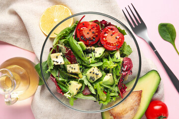 Glass bowl of tasty avocado salad with cherry tomatoes and lemon on pink background
