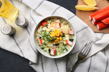 Bowl of salad with crab sticks, corn, cucumber and ingredients on black grunge background