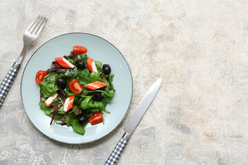 Plate of salad with crab sticks, spinach, black olives and tomatoes on light grunge background