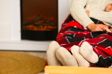 Fototapeta premium Legs of young couple in warm socks on sofa near fireplace in living room, closeup