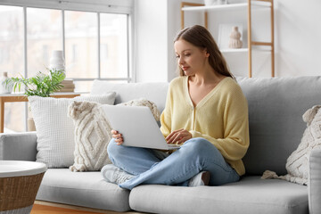 Beautiful young woman using laptop while sitting on sofa in living room