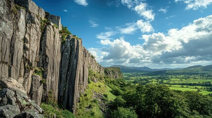 Naklejka premium Dramatic cliff face overlooking lush valley under blue sky.
