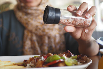 A person is skillfully seasoning a meal with pink salt inside a restaurant