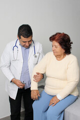 Fototapeta premium Dark-skinned Latino man medical doctor attends to elderly woman patient performs a reflex check in his office