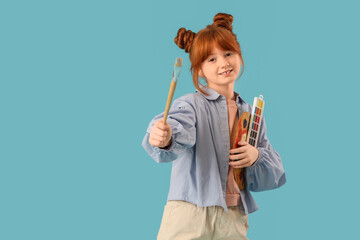 Teenage redhead girl with brush and paints on blue background