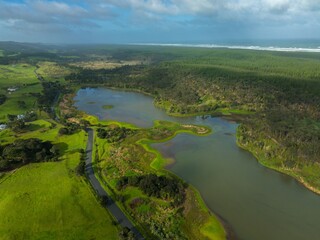 Aerial view of a tranquil lake nestled amidst lush green pastures and forests. Road winds through...