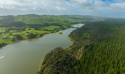 Aerial view of a lake surrounded by lush green hills and forests. Homes and farmland are visible near the water's edge.  South Head, Helensville, Auckland, New Zealand