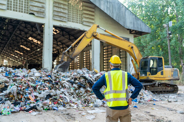 An Engineer using a laptop near a massive excavator in a recycling facility, controlling machine...