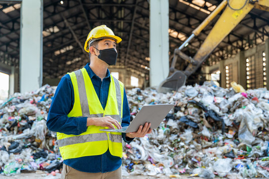 Professional engineer overseeing recycling processes with a laptop, excavator and loader machines working in the background at waste separation plant. - Powered by Adobe
