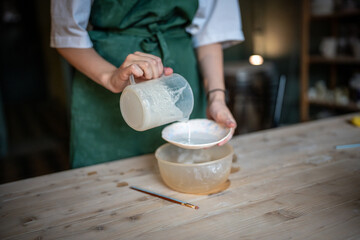 Woman potter carefully applies glaze from jug to ceramic saucer in pottery workshop. Glazing technique, handmade ceramics for sale, pottery craft, artistic job, artisan skill, handicraft production