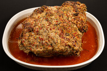 Juicy roasted pork topped with red pepper flakes and rosemary in a white bowl with flavourful Juices.