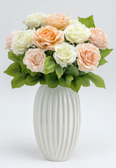 Obraz premium white ceramic vase with fluted texture holds beautiful arrangement of artificial roses soft peach and white colors, complemented by lush green leaves. This elegant floral display adds touch of