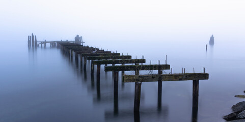 Naklejka premium Hauntingly beautiful abandoned pier stretching into misty tranquil waters evoking a sense of solitude timelessness and reflection as it merges with the serene fog creating a peaceful dreamlike scene