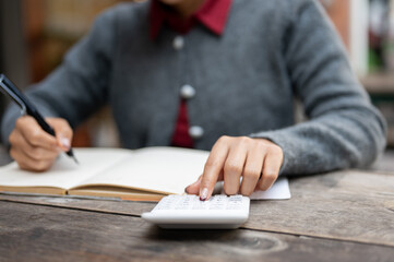A cropped image of a woman calculating her monthly expenses and bills, using a calculator.