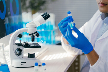 Medical scientist wearing blue gloves is closely examining a sample in a test tube while comparing it with results from microscopic analysis in a state-of-the-art laboratory