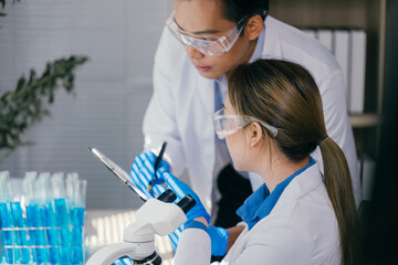 Two medical researchers wearing lab coats and protective glasses are collaborating on scientific...