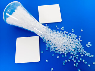 Virgin polymer granules with blue background, virgin homopolymer resin raw material poured from glass with blue background, suitable for plastic company profile product catalog design