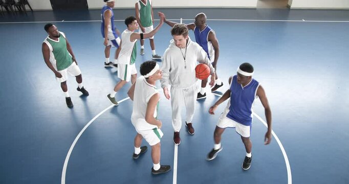 Basketball players preparing for tip-off on indoor court, coach supervising game