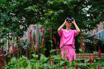 Woman wearing pink clothes using binoculars in city park