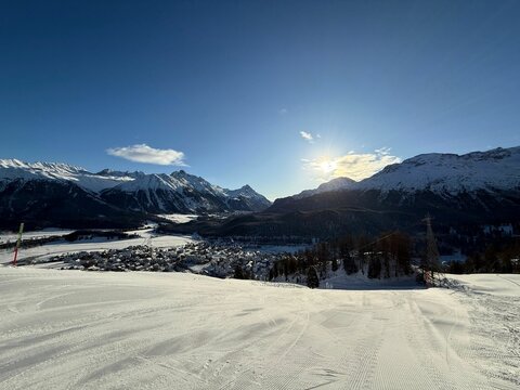 Scenic winter landscape of snowy mountains and a ski slope under a clear blue sky in Switzerland.