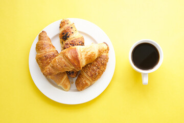 Coffee cup and fresh croissants on yellow background