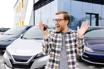 Emotional guy holding key in hand and smiling at camera. Man showing key from his new electric car....