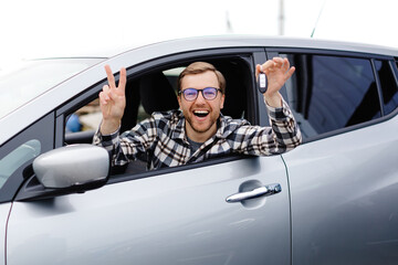 Excited young man showing a car key, sitting inside his new vehicle