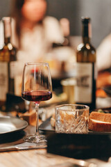 Glass of rich red wine served with cheese plate and fruits on dark wooden background. Appetizers table with wine glasses, rustic style table setting in winery