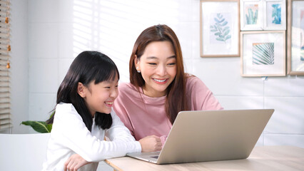 Mother and Daughter Smiling and Using Laptop Together at Home. Family Bonding, Online Learning, Lifestyle or Entertainment in Comfortable Living Room.