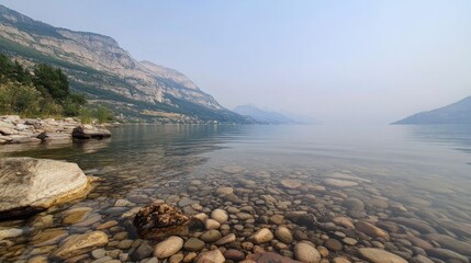 Serene lakeside view with smooth stones and mountains in the background.
