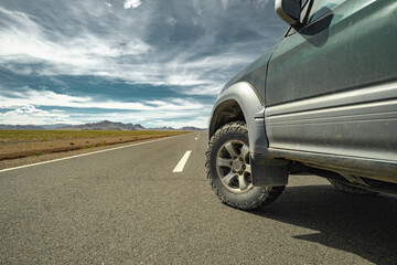 An off-road vehicle on mud tires stands on asphalt against the backdrop of the steppe, mountains and sky. Mud tires on asphalt in the steppe. A car for traveling. Rubber for travel.