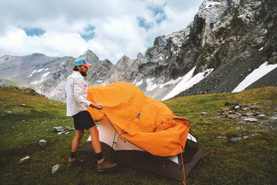Man setting up tent camping gear in mountains hiking travel adventure outdoor, healthy lifestyle summer active vacations with climbing equipment