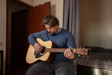 Obraz premium Focused Man Practicing Acoustic Guitar at Home, guitarist strumming strings in bedroom, learning instrument as hobby