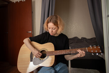 Woman playing guitar, strumming strings as part of her musical hobby, learning the skill indoors.