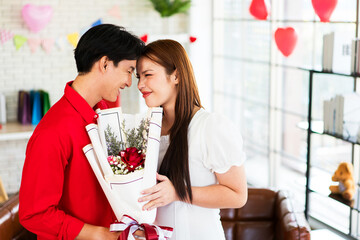 A couple shares a romantic moment, exchanging smiles as one presents a bouquet of flowers in a cozy, decorated space.
