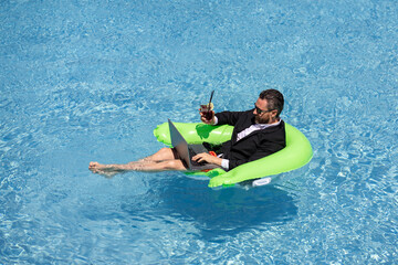 Freelance work, distance online work, e-working. Summer business. Business man in suit drink summer cocktail and using laptop in pool. Businessman dreams on summer business in swimming pool water.