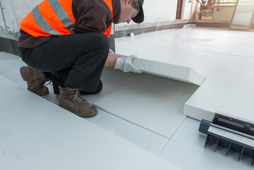 Professional worker is laying styrofoam insulation sheets on house terrace with roof function for...
