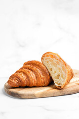 Croissants on wooden cutting board on white marble background