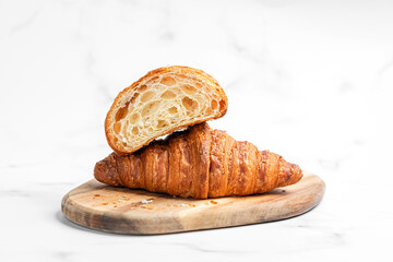 Croissants on wooden cutting board on white marble background