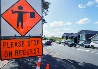 Please Stop on Request road sign by the road. Cars travelling on the road. Roadworks in Auckland.