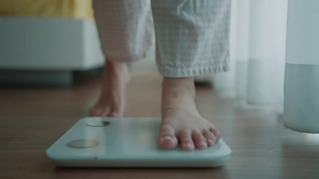 Close up a woman's bare feet stepping onto a digital weighing scale in the morning at home. Healthy lifestyle and weight awareness concept