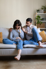 Front view of man comforting depressed wife sitting on the couch at home living room. Vertical...