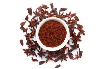 A bowl of Organic Star anise or Chakra Phool (Illicium verum) powder, placed over a heap of whole star anise fruit. Isolated on a white background.