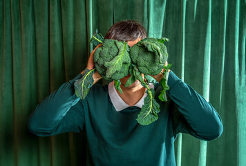 Man hold broccoli in front of his face against background of green curtains. Vegan nutrition...